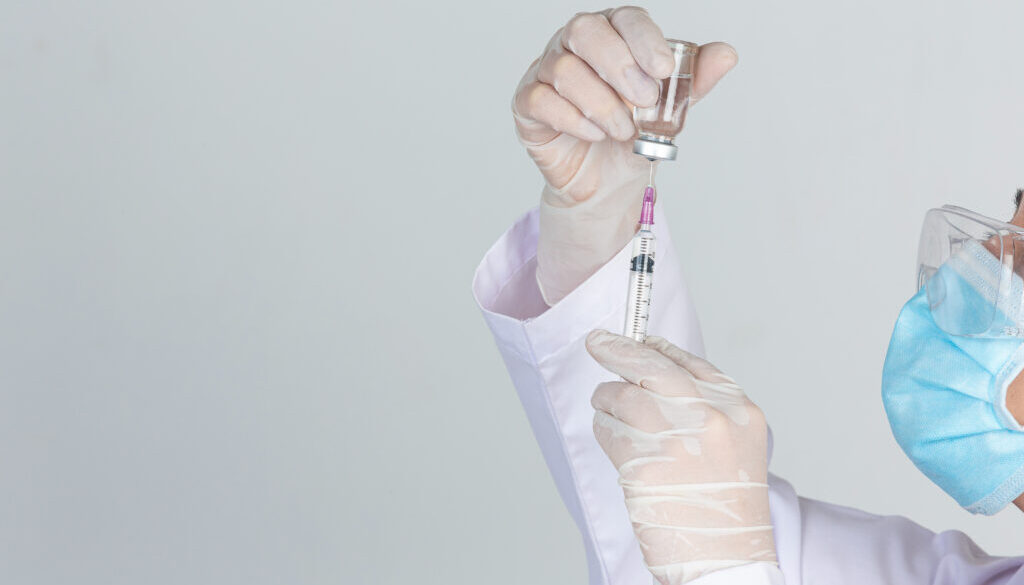 Young doctor is holding hypodermic syringe with vaccine vial