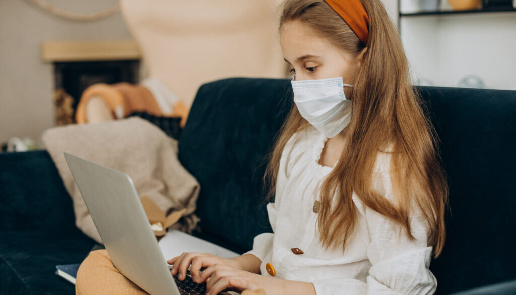 School girl studying at home wearing mask, distant learning